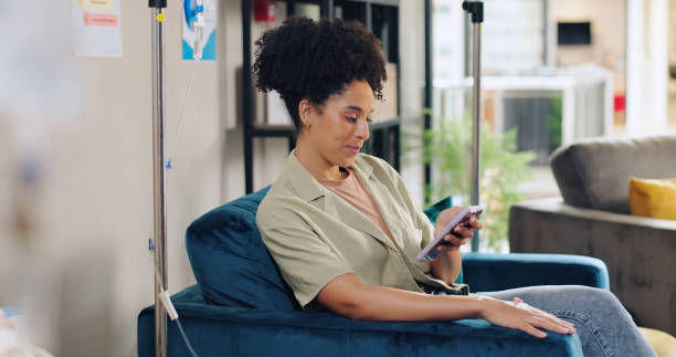 A woman scrolls her phone while receiving an IV treatment.
